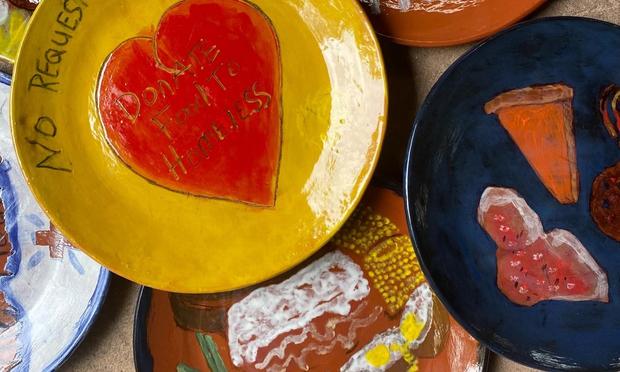 A color photo of glazed ceramic plates, one painted with a red heart on a yellow background, two others with food