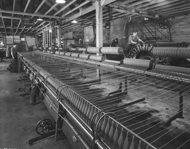 A large mill machine which seems to be taking spun wool and making it into shorter/smaller bobbin like devices. It's a long machine with several dozen spools being handled at once.