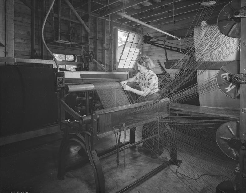 A woman works on a weaving or spinning device of some kind.